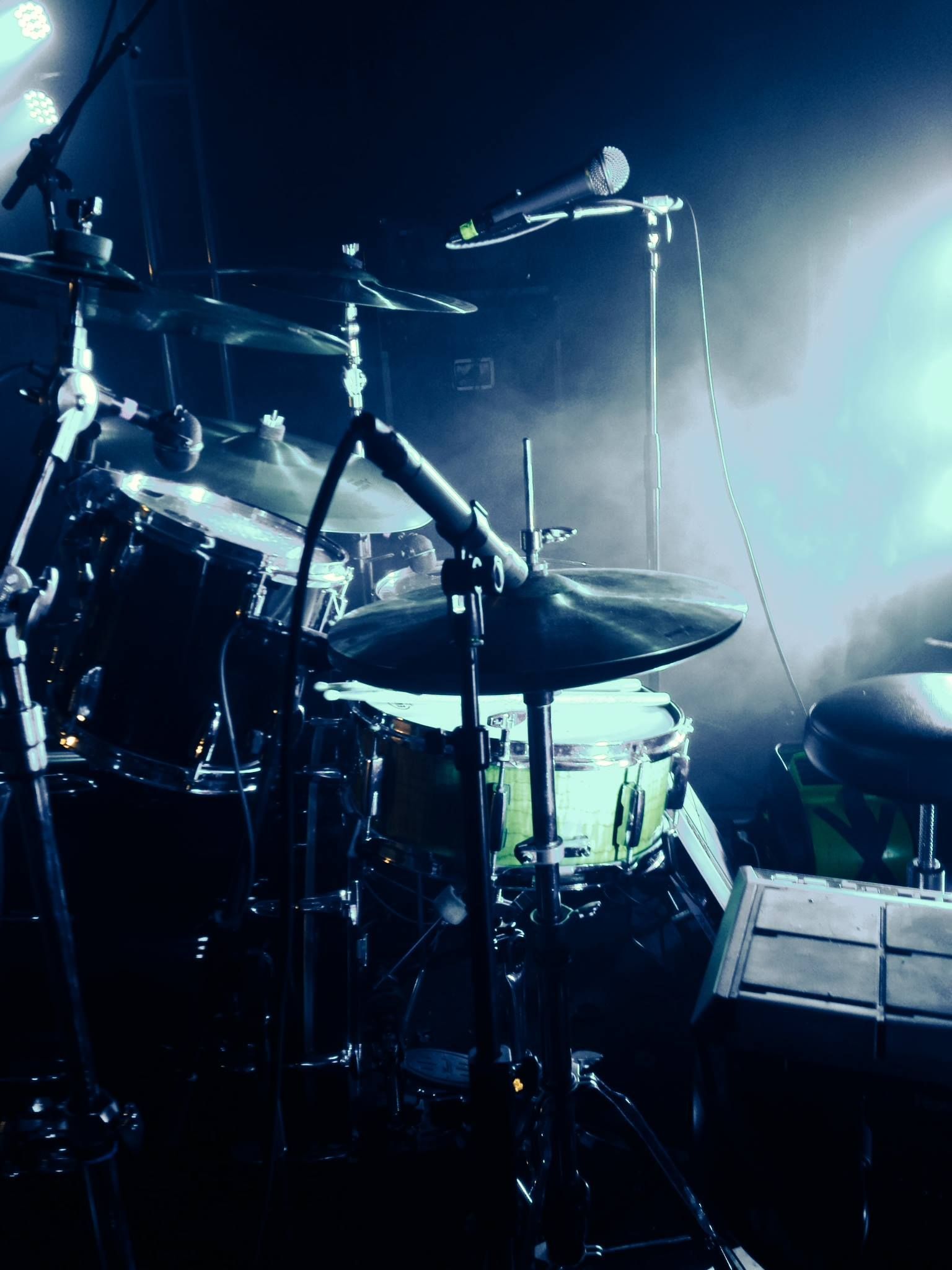 Drum kit on a dim blue-lit stage with microphones and bright concert lights