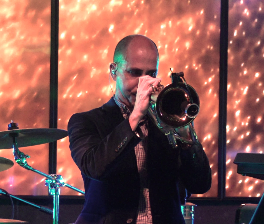 Musician playing a trumpet on stage with warm orange lights in the background