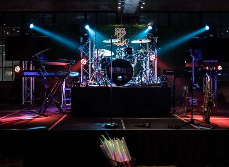 Empty concert stage with drum kit and keyboards lit by blue and red stage lights