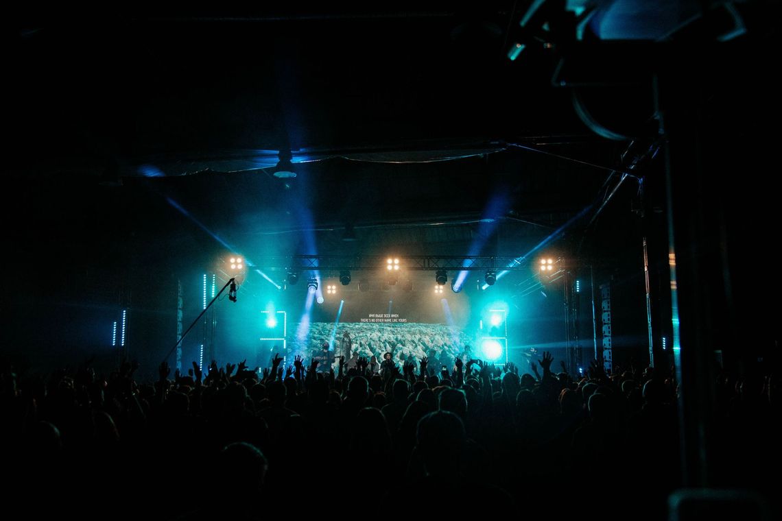 Concert crowd in a dark venue, lit by blue stage lights and bright spotlights.