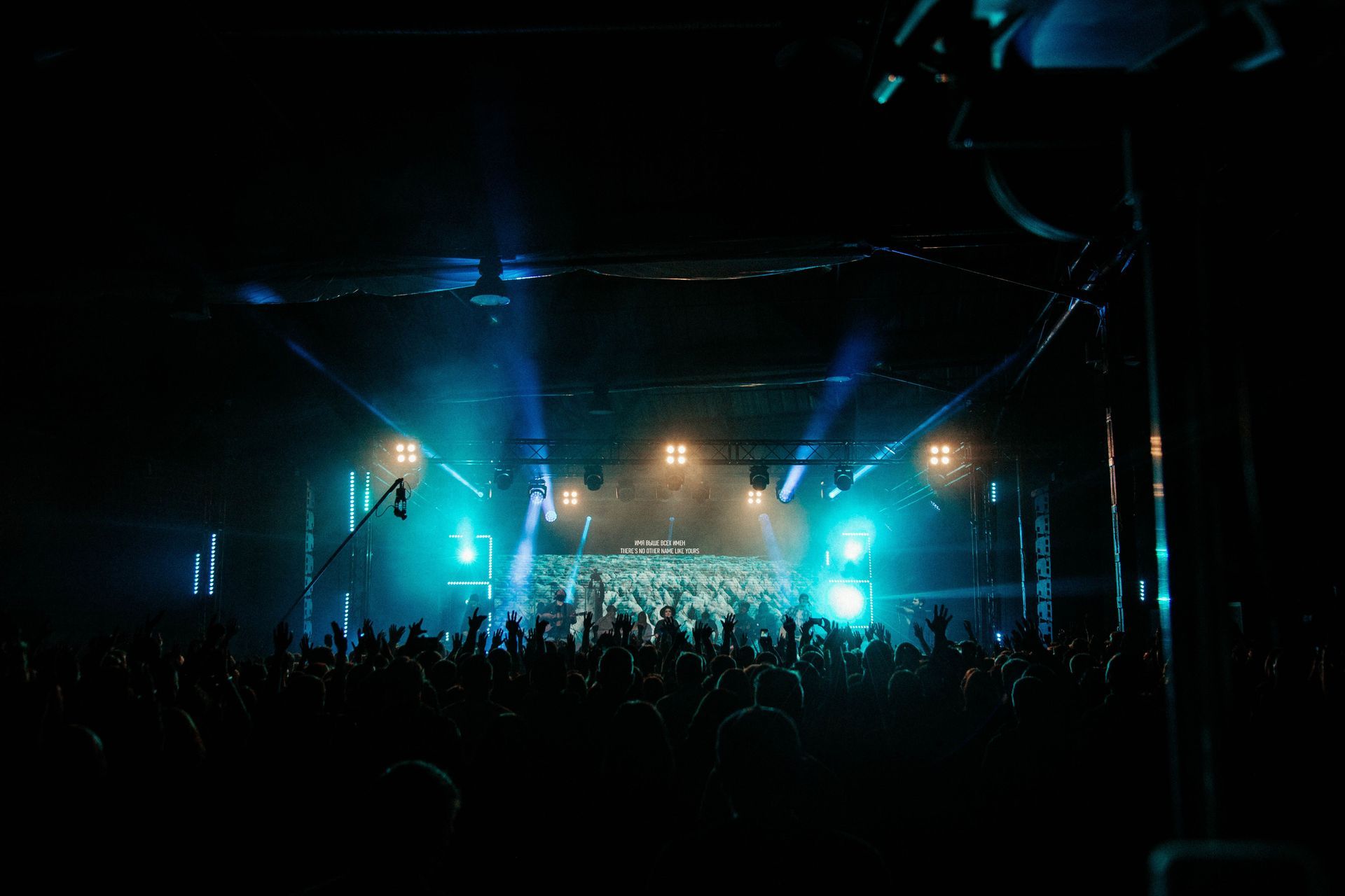 Concert crowd in a dark venue, lit by blue stage lights and bright spotlights.