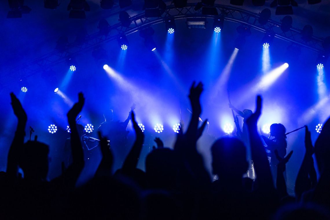 Crowd cheering at a concert under blue stage lights with raised hands and silhouettes