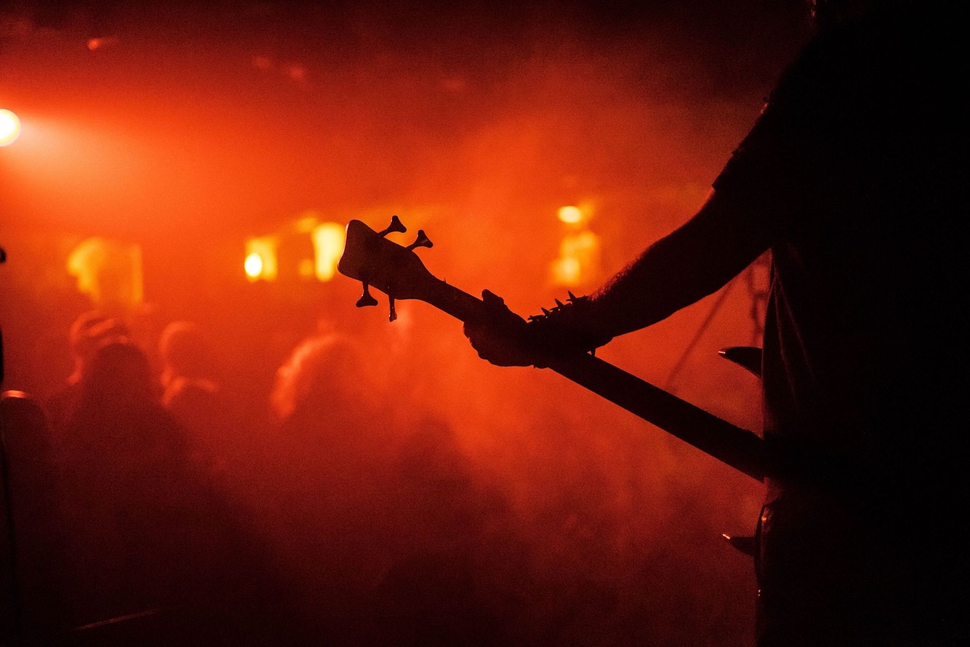 Silhouetted guitarist onstage in orange-red concert lighting, facing a hazy crowd