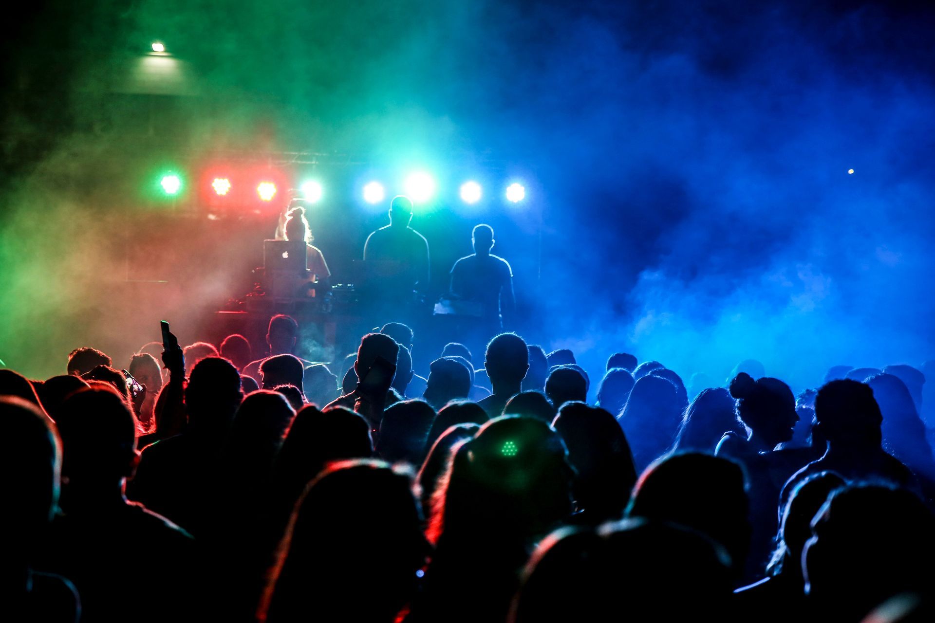 Concert crowd silhouetted under blue, red, and green stage lights with performers in the background