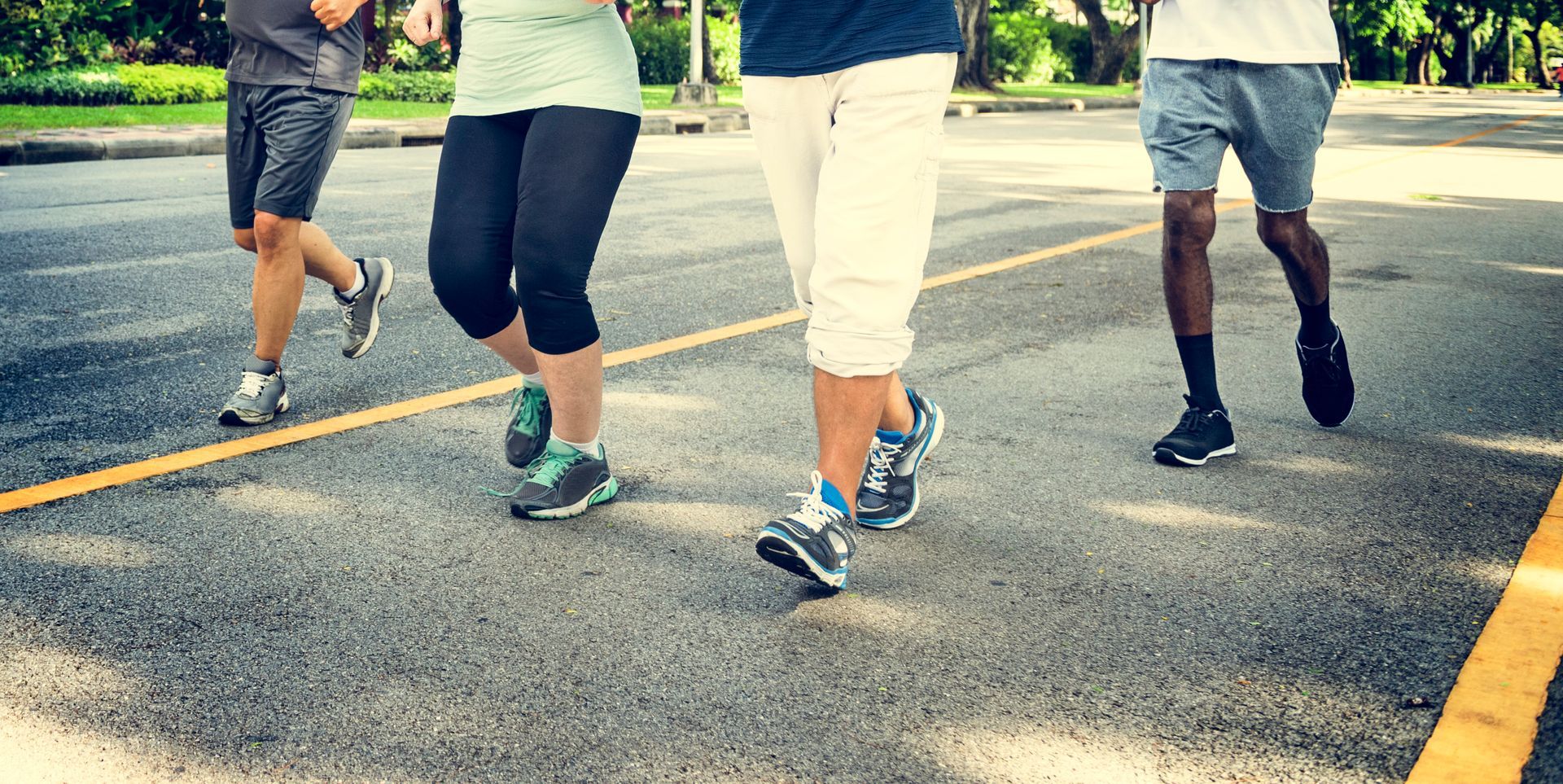 Four people running on a paved road with yellow lines. They are wearing athletic clothes.