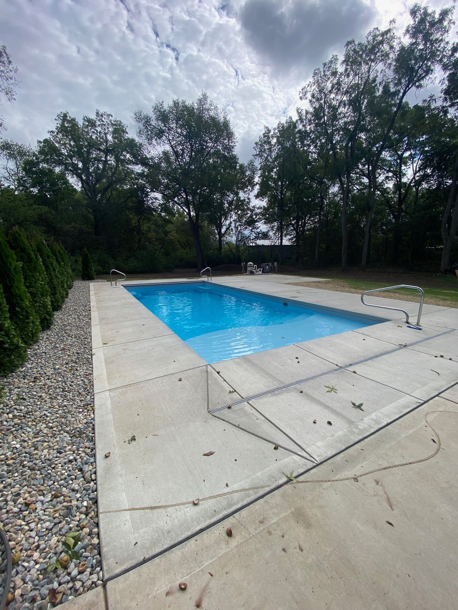 A large swimming pool is surrounded by trees on a cloudy day.