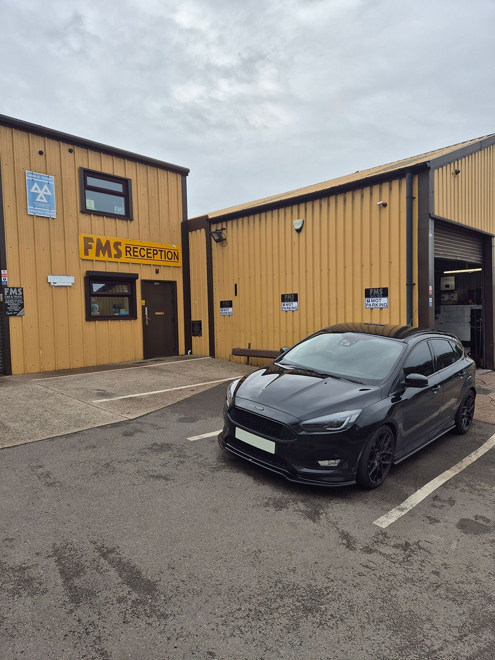 A black car is parked in front of a yellow building.