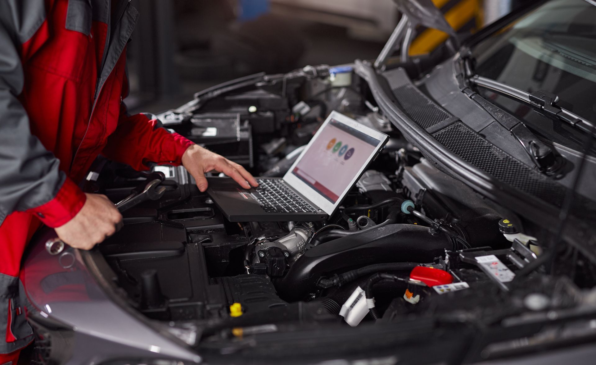 A mechanic is working on a car engine with a laptop.
