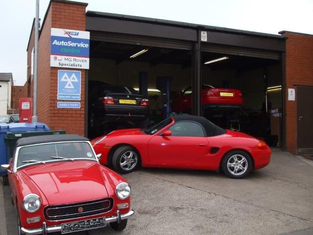 Two red sports cars are parked in front of a building that says autoservice