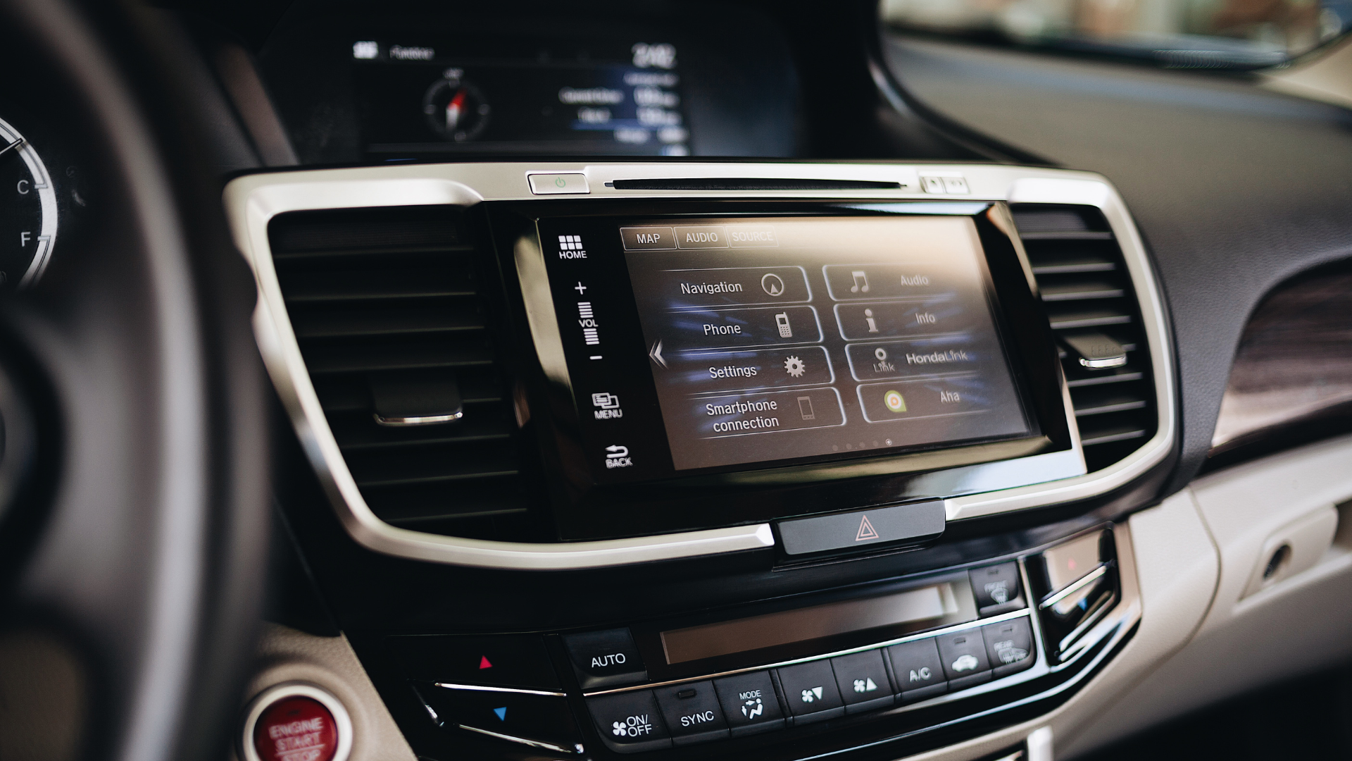 Car dashboard center console with touchscreen display, vents, and climate controls in a black interior.