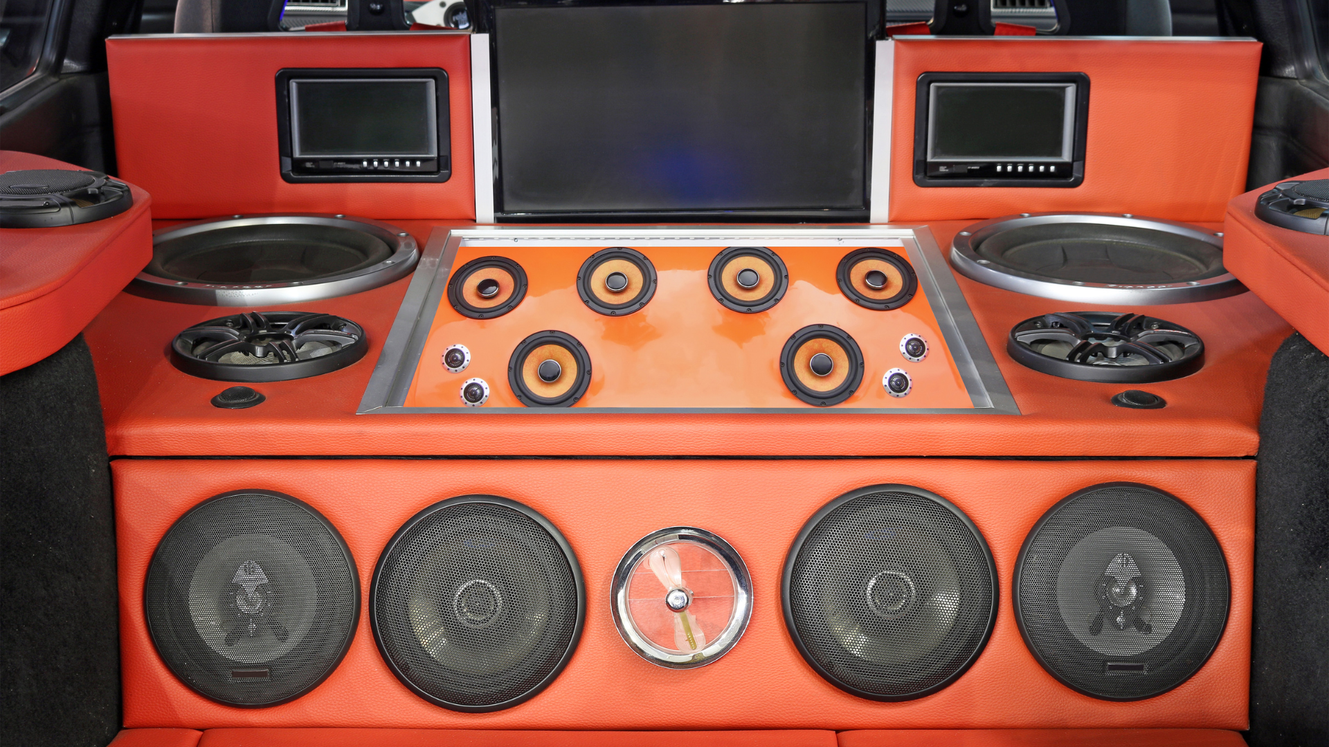 Orange custom car audio setup with multiple speakers and two small screens in a trunk-like display