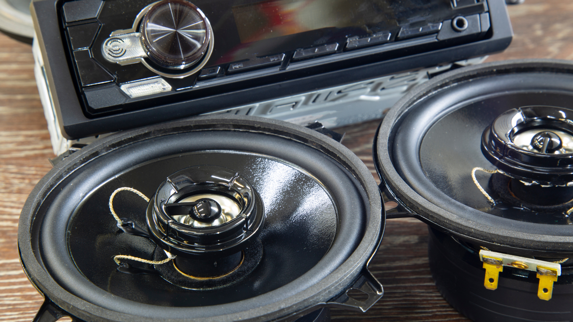 Two black car speakers and a stereo head unit on a wooden surface