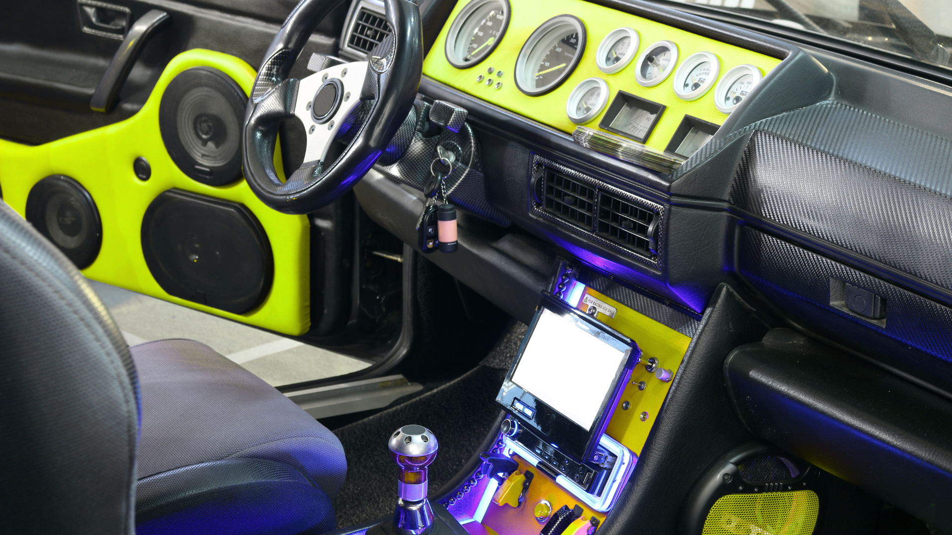Customized car interior with neon yellow dashboard, multiple gauges, black seats, and purple-lit center console