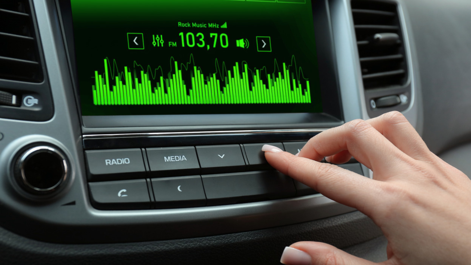 Hand adjusting a car radio display showing green audio waveform and station 103.70 FM