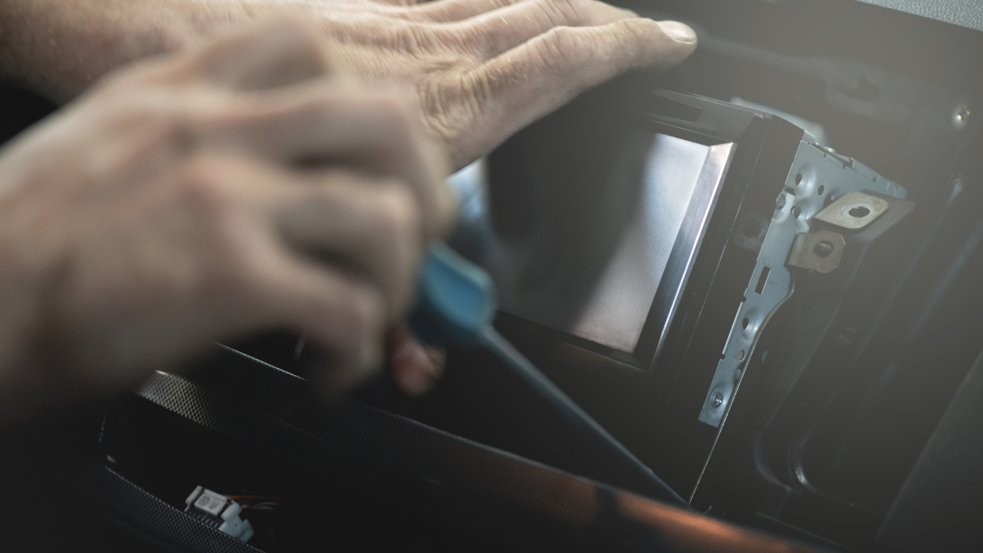 Hands holding a screwdriver inside an opened car dashboard panel.