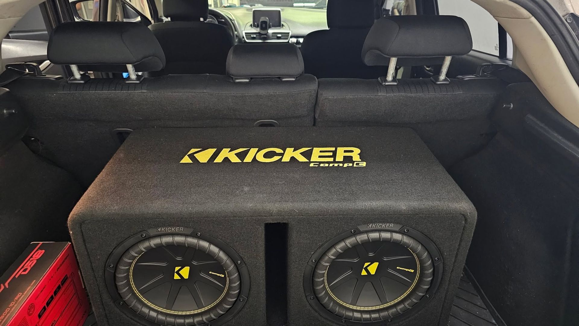 Kicker subwoofer box in the back of a car trunk, black with yellow logo and dual speakers.