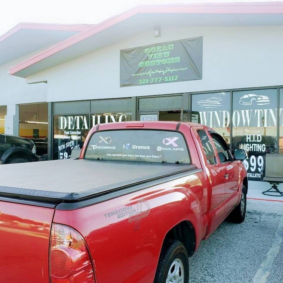 Red pickup truck parked outside a window tint shop with “window tinting” signs.