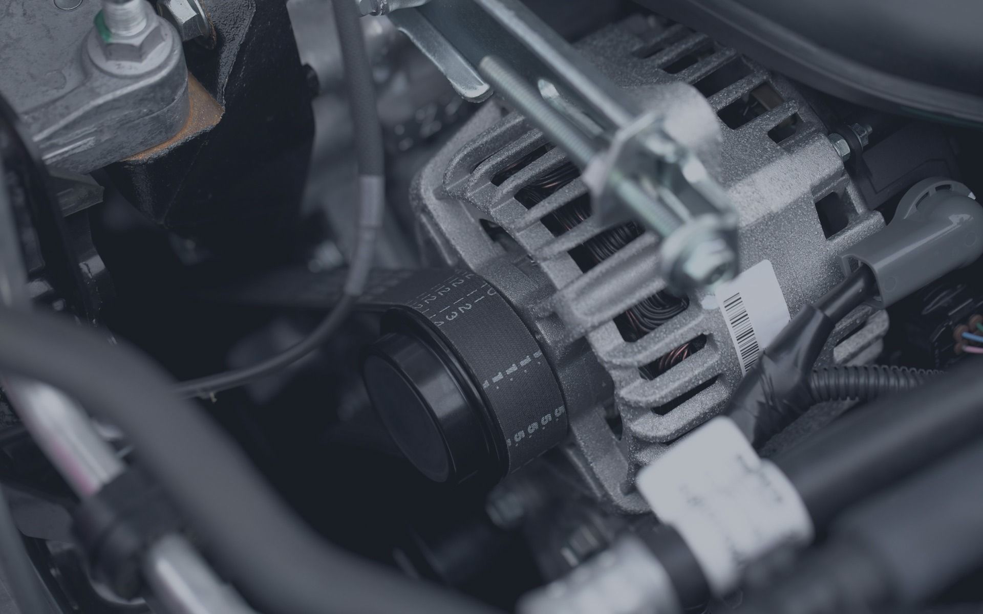 Close-up of a car engine alternator with belts and wiring underneath the hood
