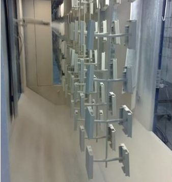 Parts hanging on a rack being spray-painted with white paint in a factory setting.