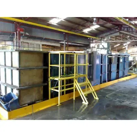Large industrial metal finishing tanks in a factory setting, with yellow safety platforms and walkways.