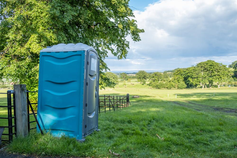 A Blue Portable Toilet is Sitting in the Middle of a Grassy Field — Coffs Coast and Country Temp Fence in Sapphire Beach, NSW