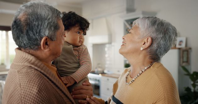 Three people chatting in a bright kitchen, with a child held between two smiling adults