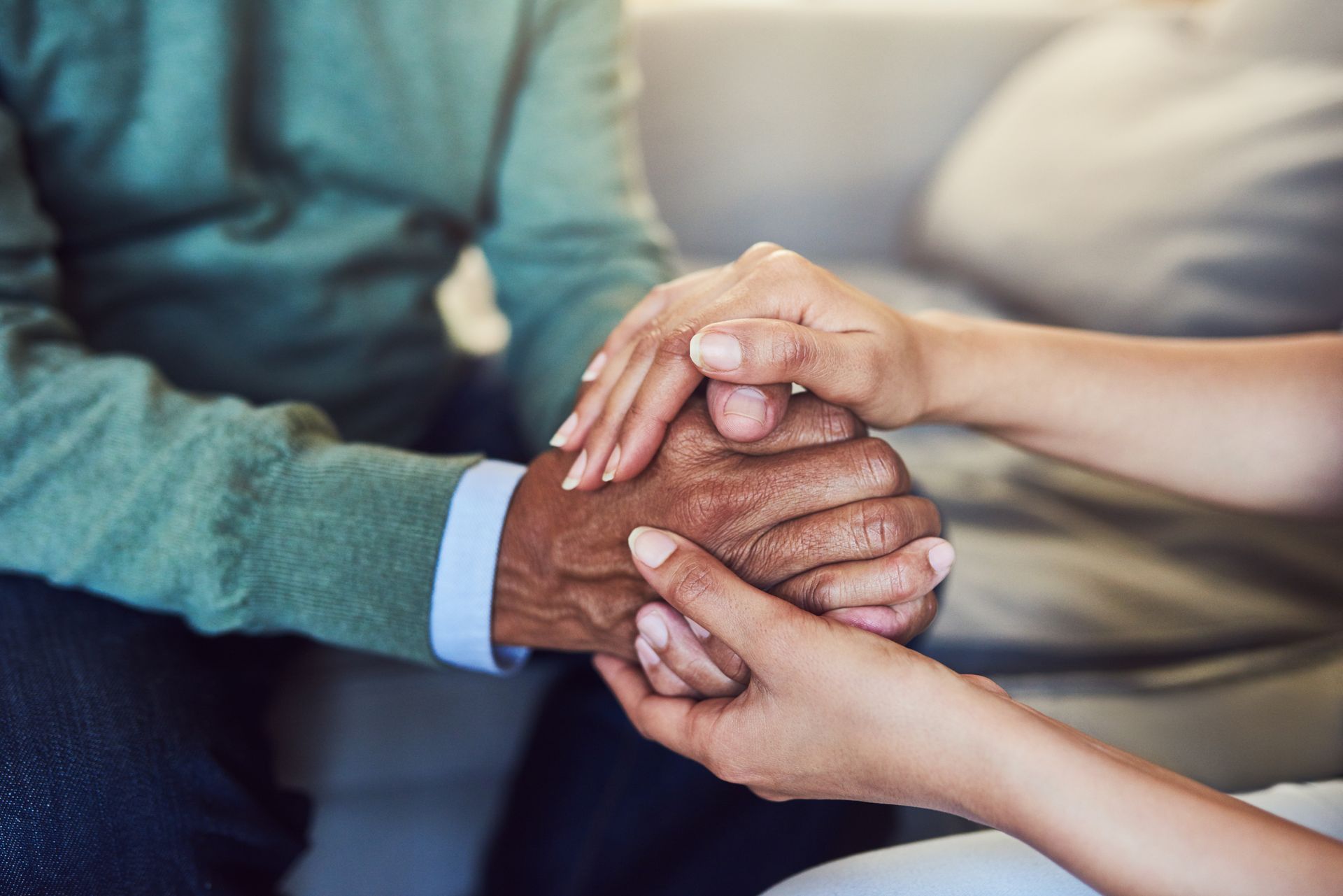 Hands of two people gently stacked together in a supportive gesture on a couch