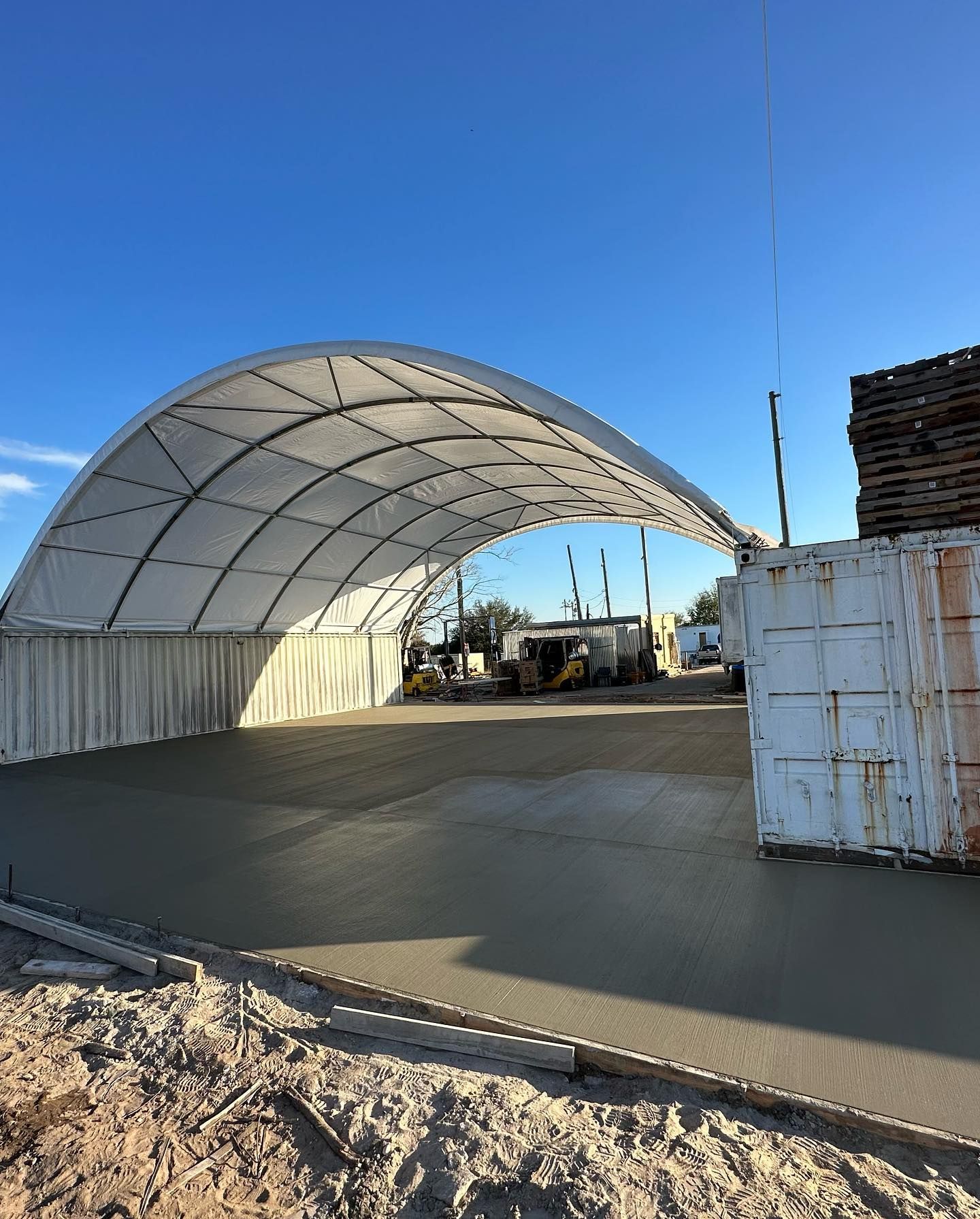 Concrete being poured under an arched, white-covered structure. Construction site with blue sky.