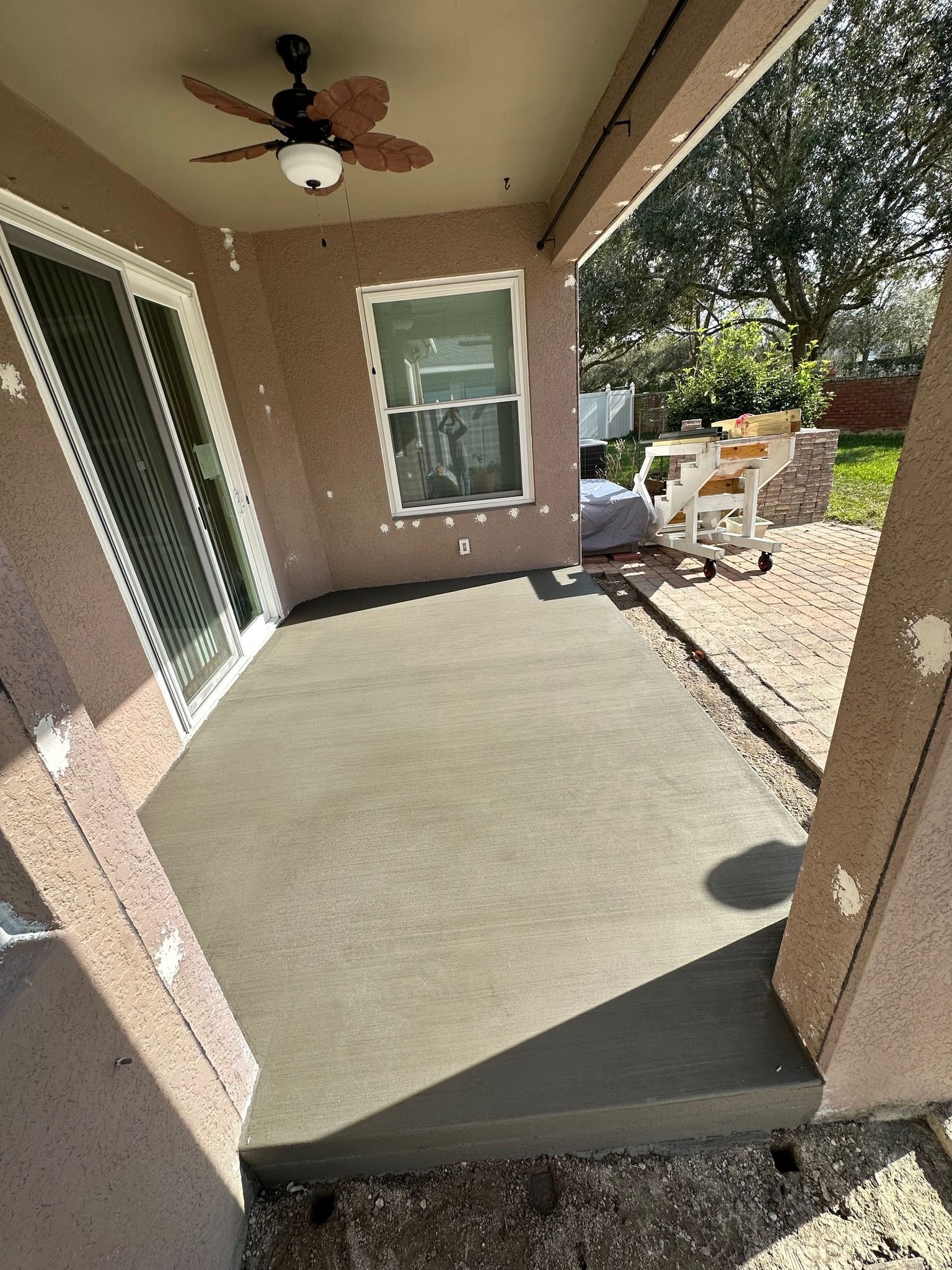 Covered patio with freshly poured concrete, a sliding glass door, and a window.