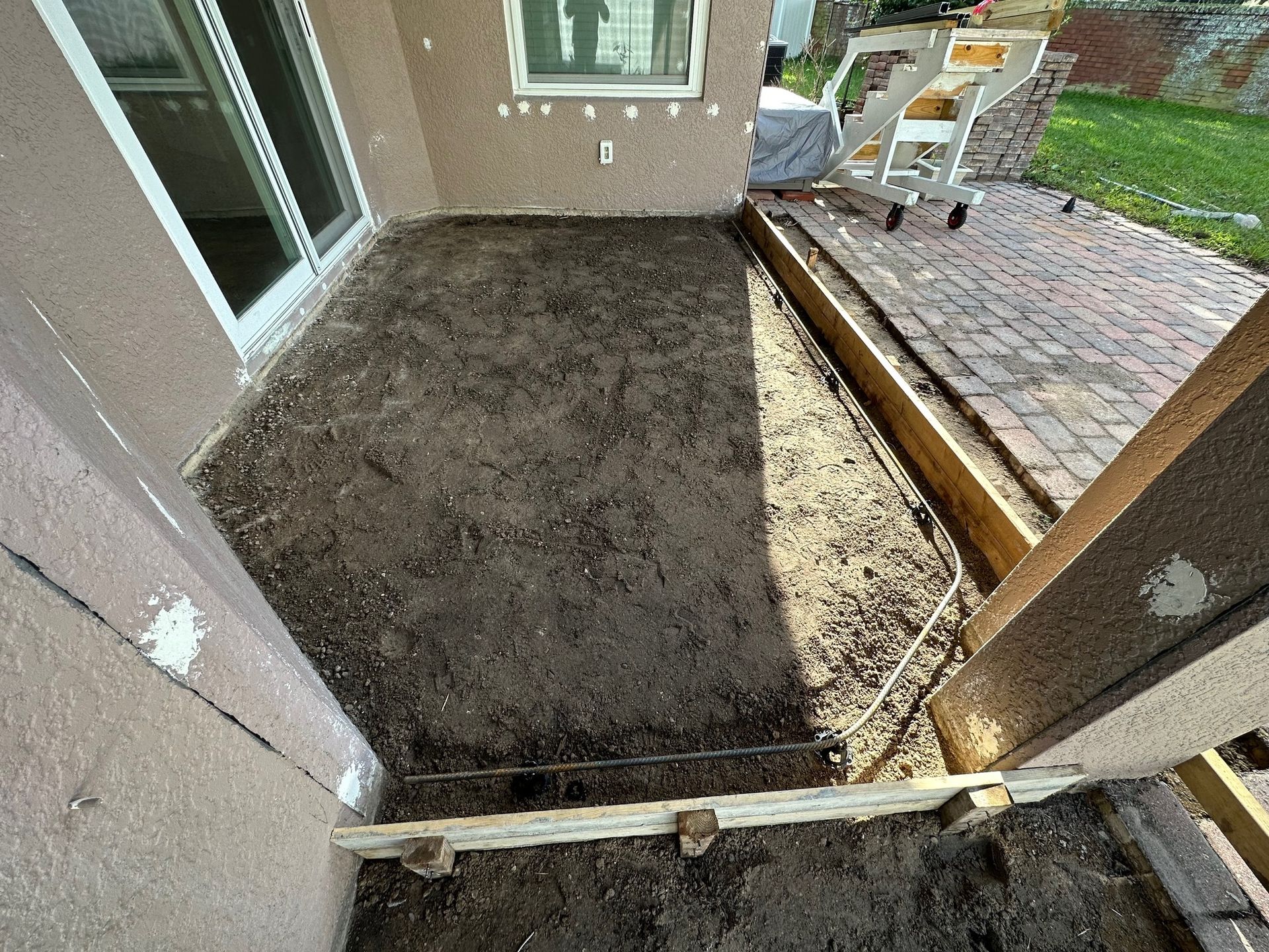 A dirt-filled patio section next to a brick patio, prepared for construction. Wooden framing visible.