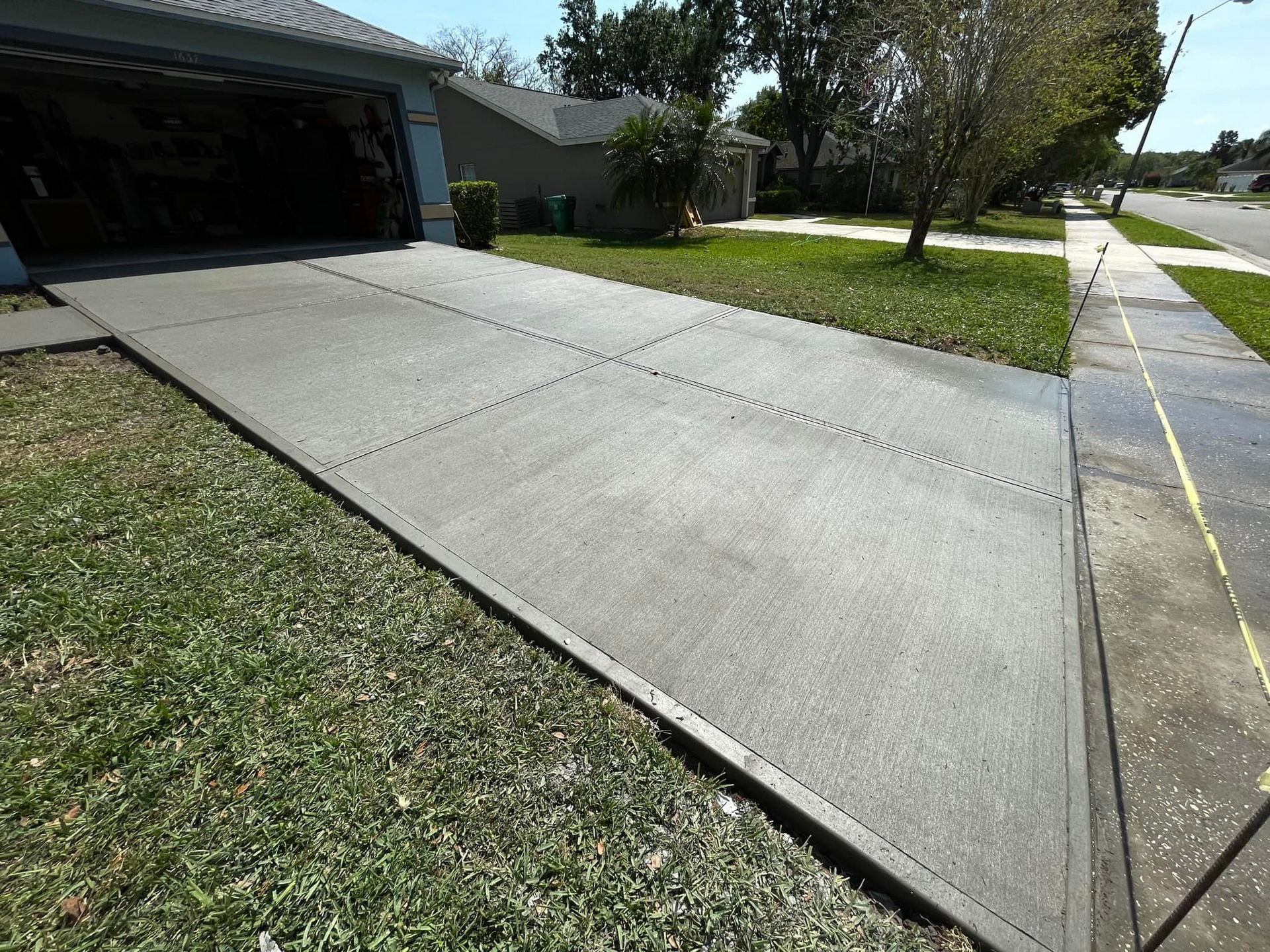 Concrete driveway leading to a garage, beside a grassy lawn and sidewalk.