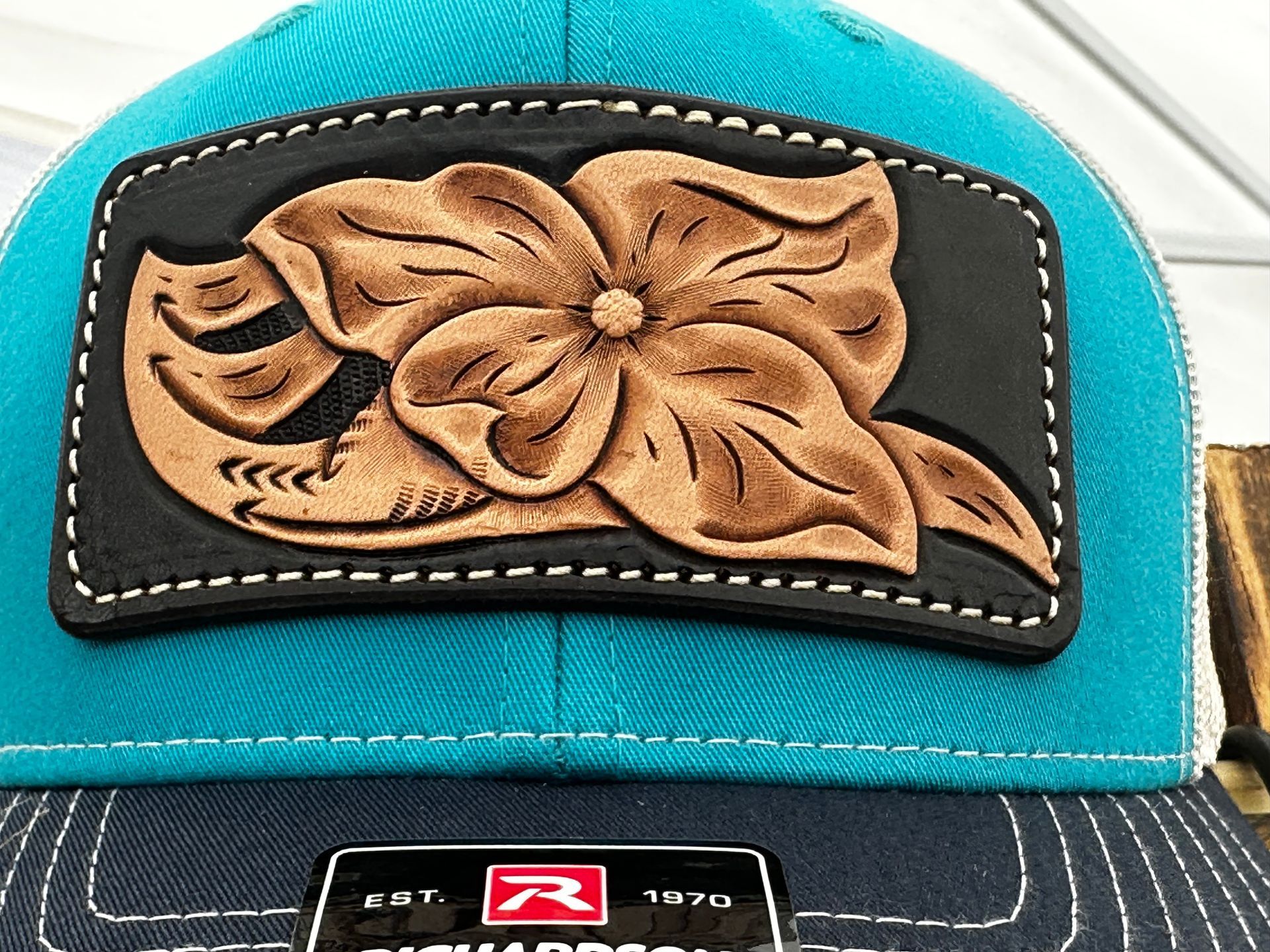A TOOLED HAT PATCH OF A FLOWER AND SCROLL.  TEAL HAT