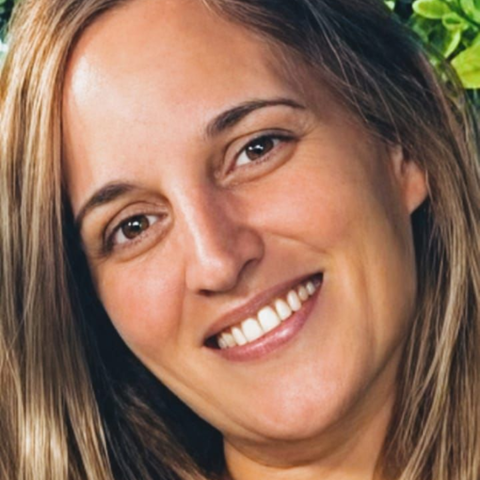Mujer sonriente con cabello castaño al aire libre, retrato en primer plano con luz natural.
