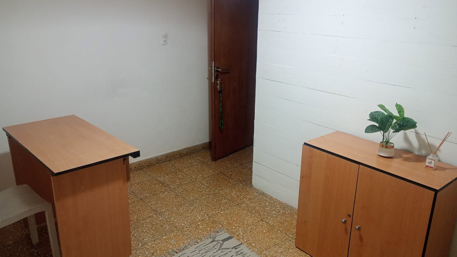 Habitación pequeña y vacía con dos armarios de madera, un escritorio, paredes blancas y una puerta cerrada.