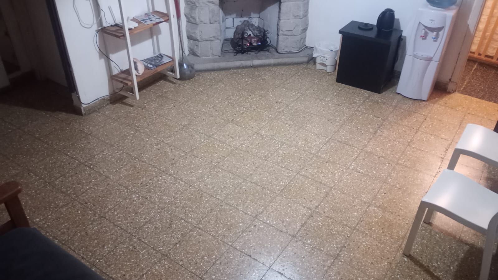 Sala de estar con suelo de baldosas, chimenea, estanterías, armario negro y dos sillas a la derecha.