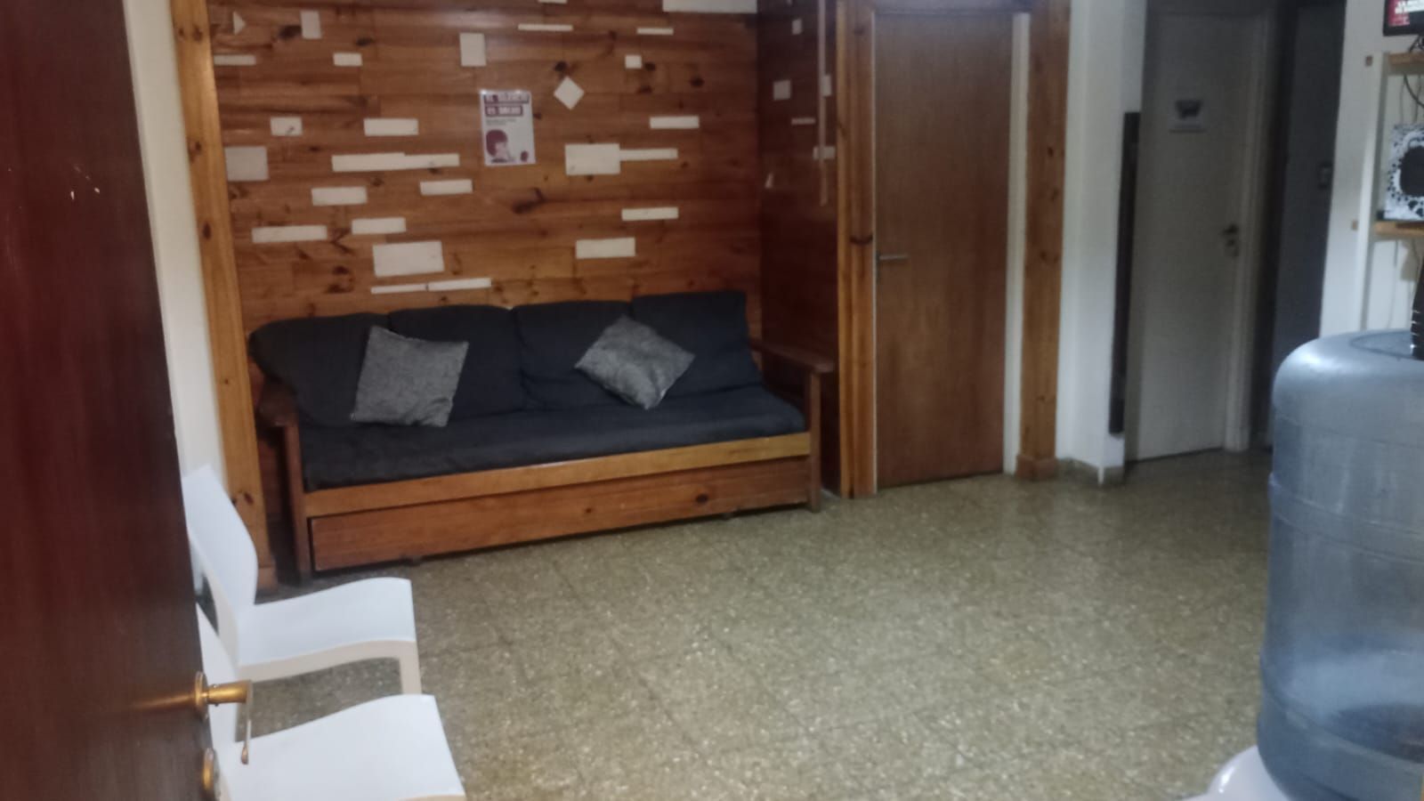 Habitación pequeña con un diván de madera, una pared decorativa de ladrillo visto, sillas y suelo de baldosas.