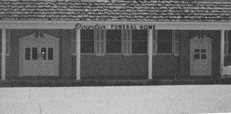 Small brick funeral home with dark green awnings and a front door on a snowy street