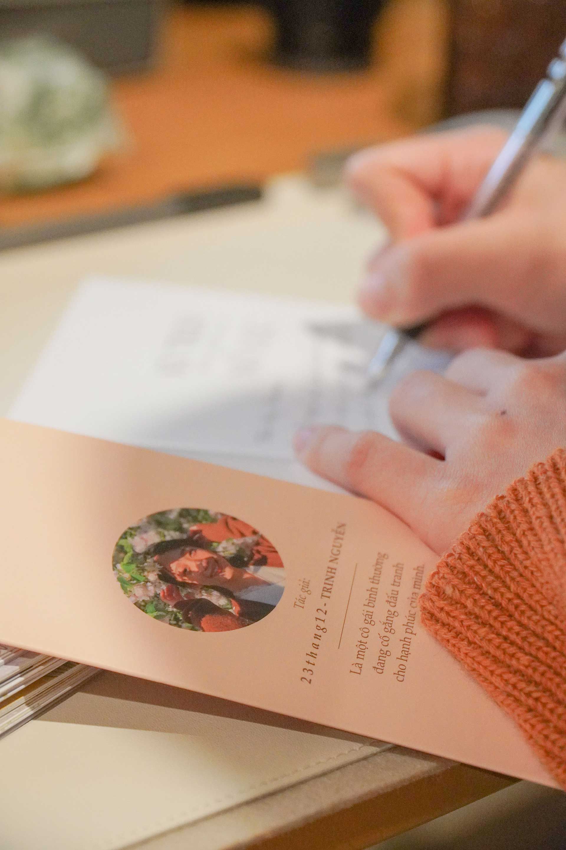 Hand writing on a card at a table, with a circular floral design on the page.