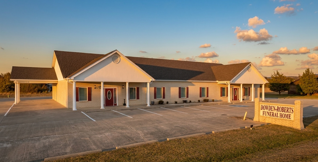 Single-story white community building at sunset with a gravel lot and roadside sign.