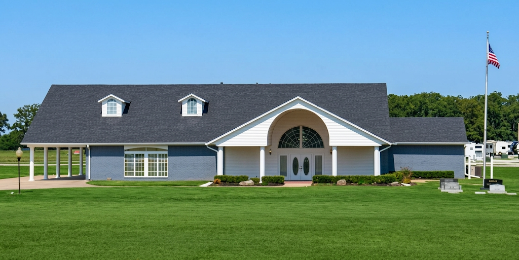 Small white building with a dark roof and arched entrance, set on a green lawn under a blue sky.