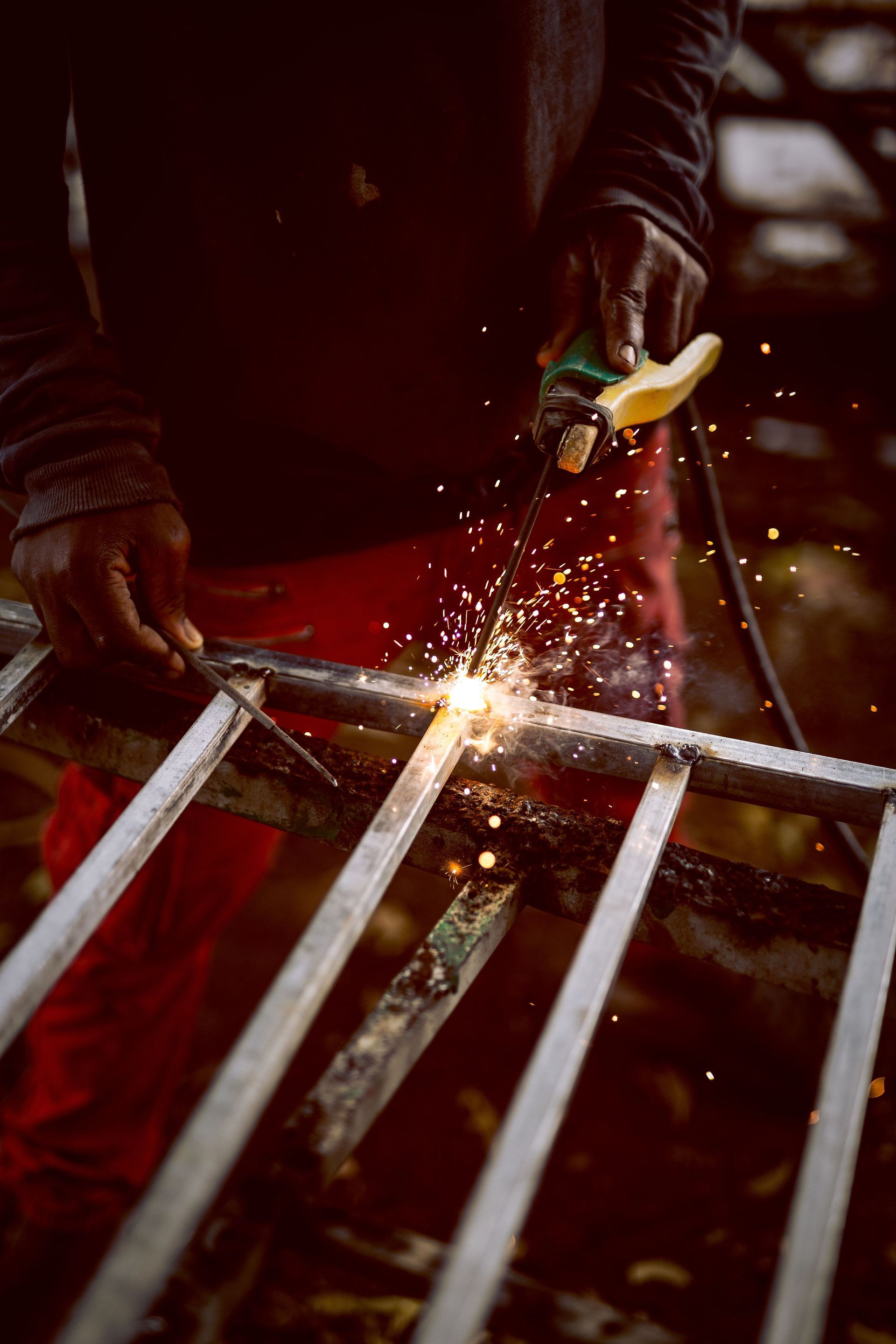 Worker cutting metal with a grinder, sparks flying over a red ladder-like frame.