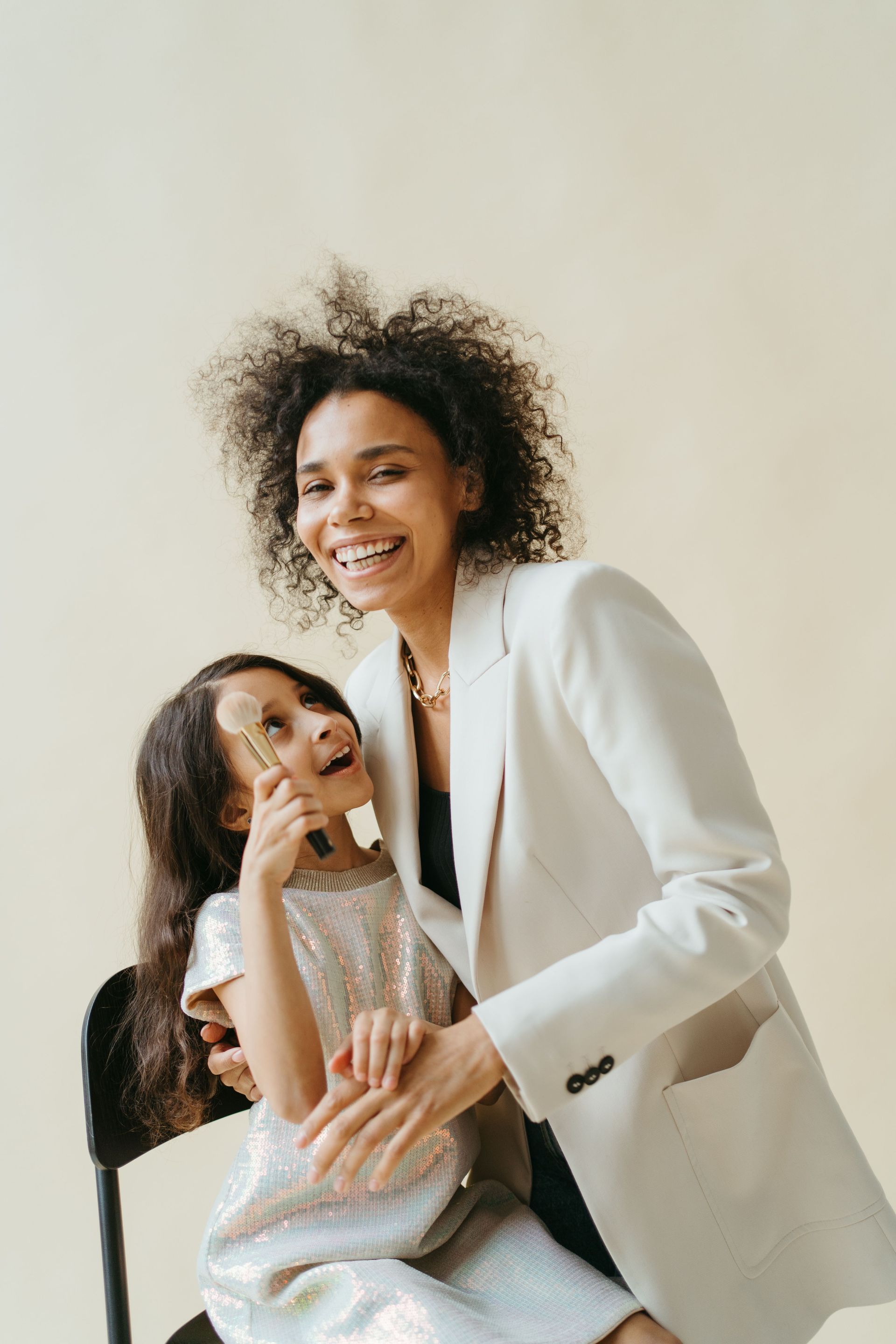Two smiling people in white blazers pose together against a light background.
