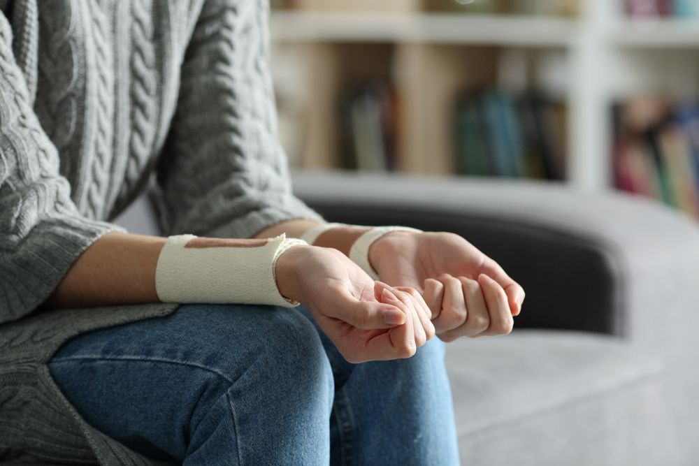 Person seated on a couch with a white bandage wrapped around their wrist and hand