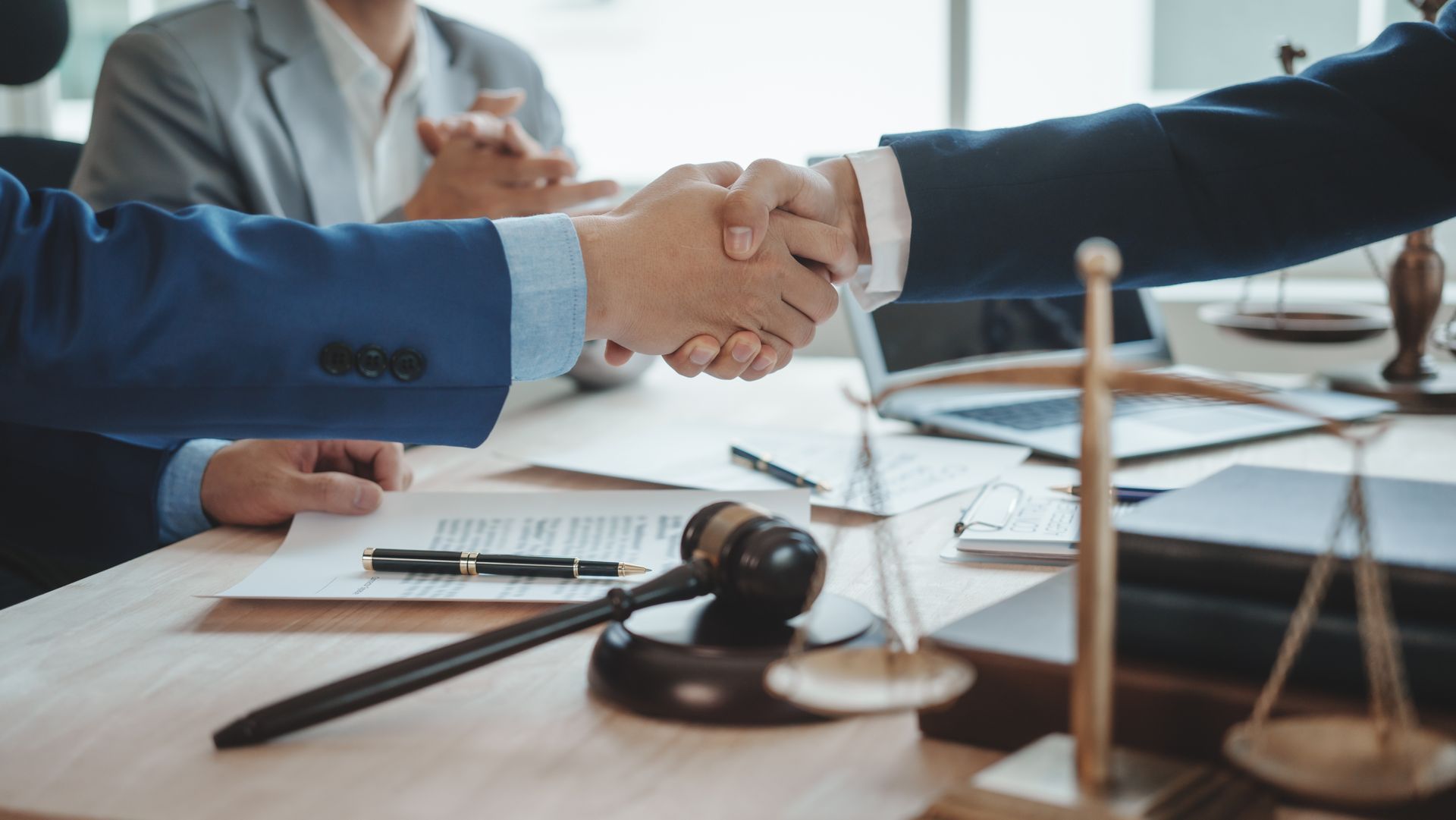 Businesspeople shaking hands over a desk with a gavel, documents, and a scale of justice