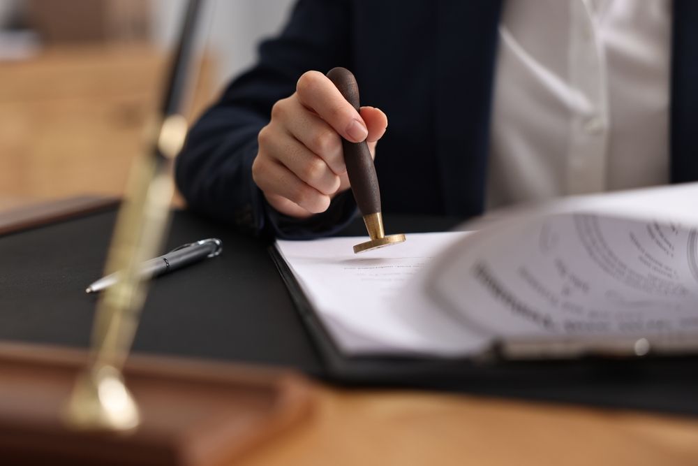 Hand signing a document on a desk beside papers and a pen
