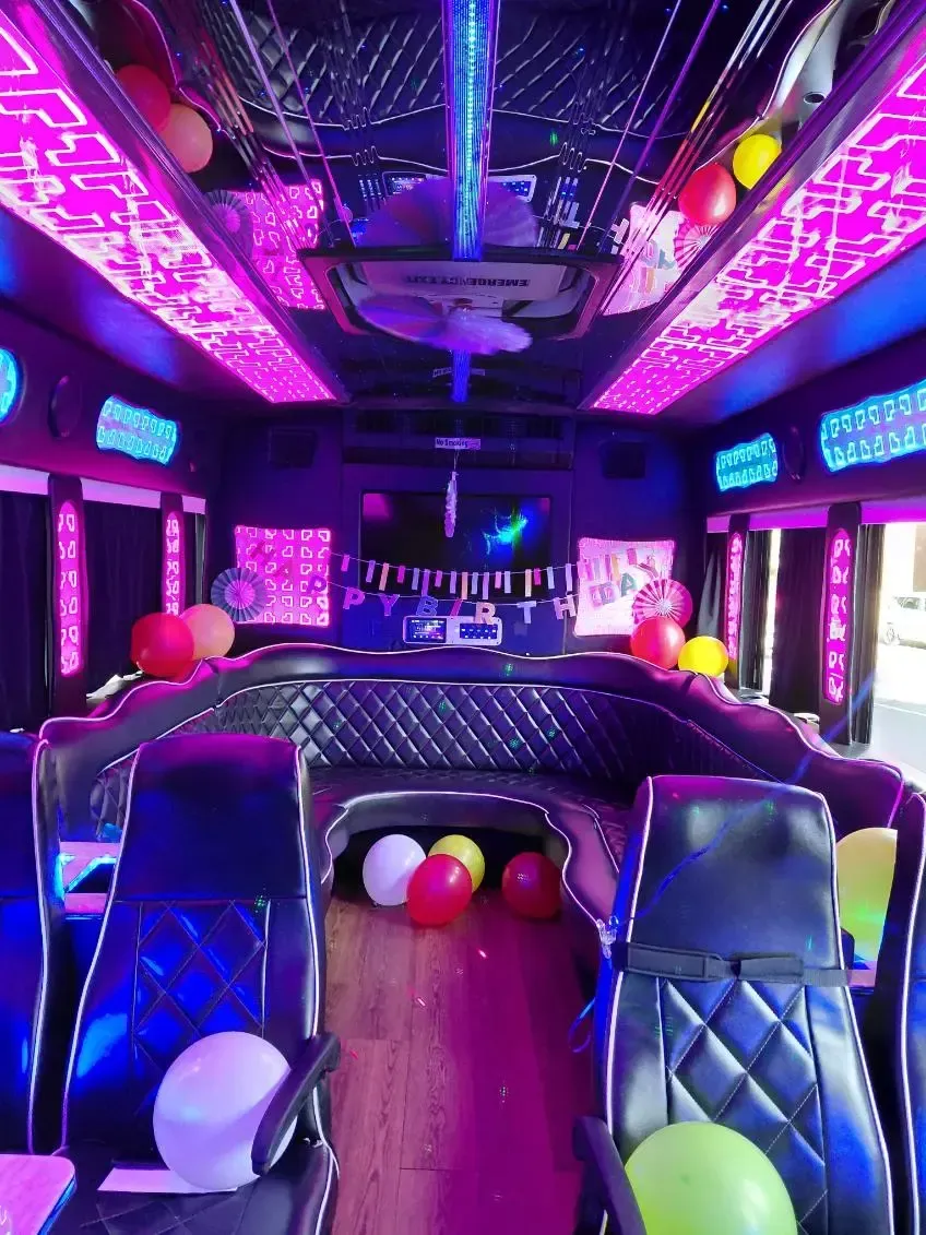 Neon-lit party bus interior with purple lighting, balloons, and rows of seats