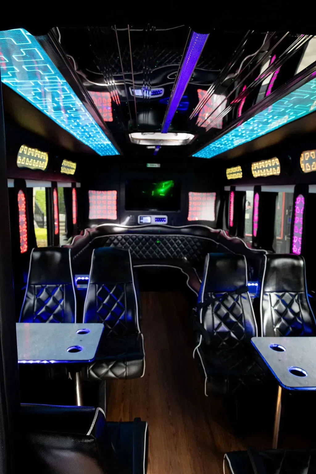 Neon-lit party bus interior with rows of black seats, LED ceiling lights, and wooden floor