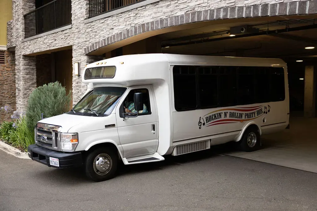 White shuttle bus parked under a building overhang, side door open and ready for passengers.