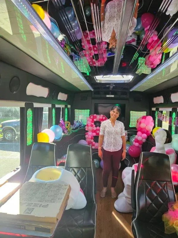 Decorated party bus interior with pink and white balloons; a woman stands in the aisle.