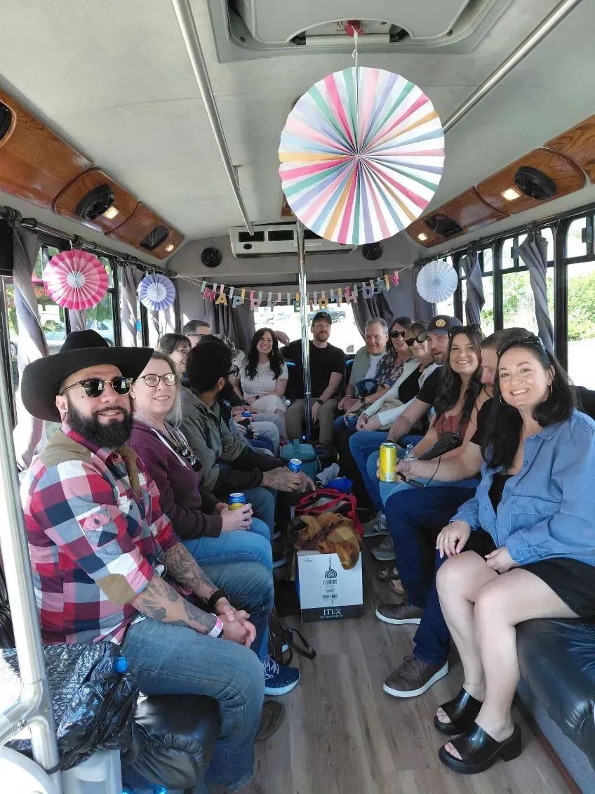 Passengers seated inside a bus, many holding drinks, with colorful decorations hanging from the ceiling.
